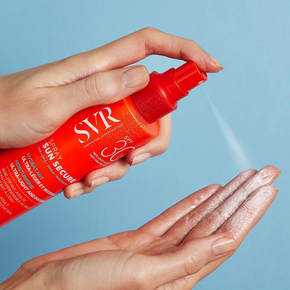 Mano che spruzza lo spray solare SVR Sun Secure SPF30 dal flacone arancione su un palmo aperto, su sfondo azzurro.