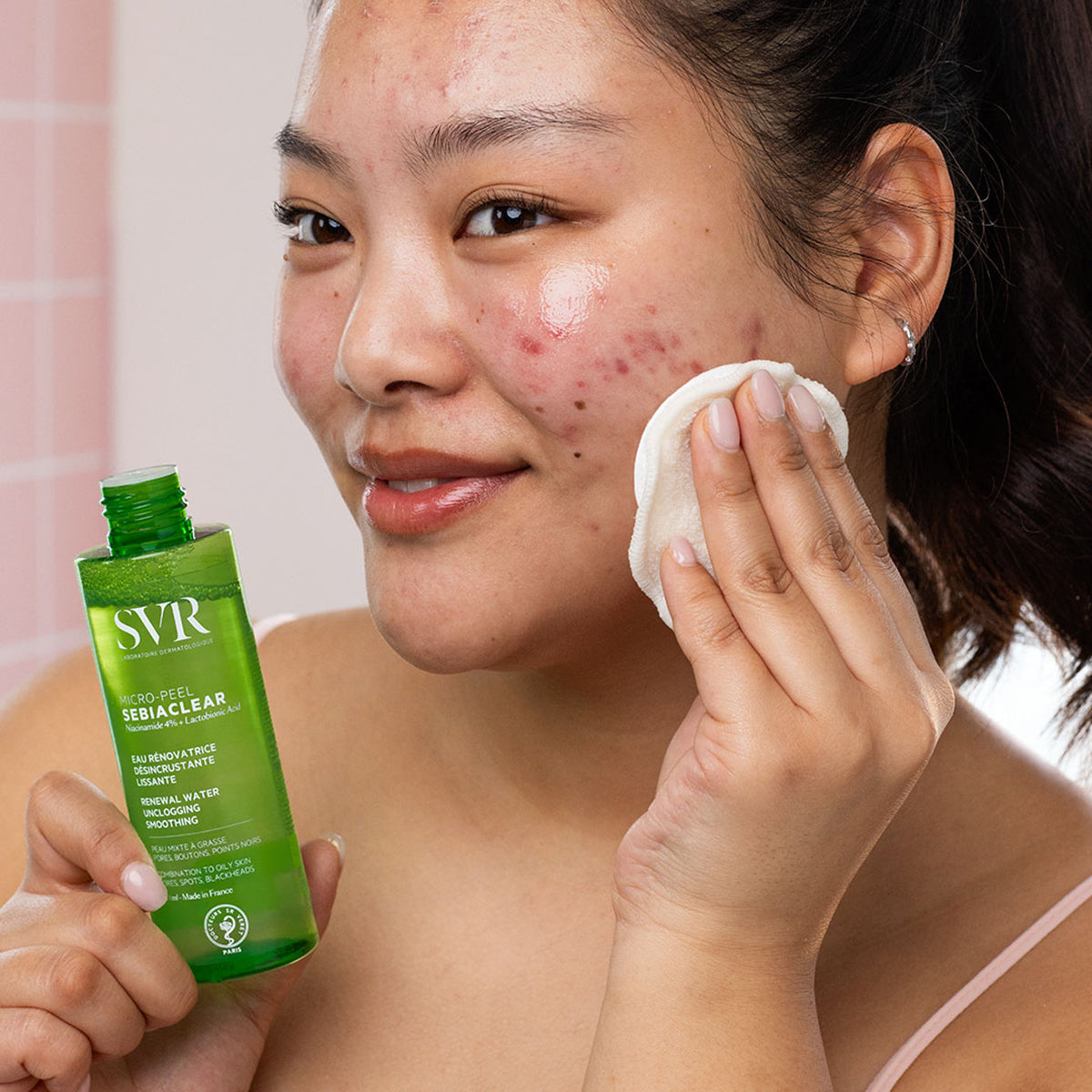 Donna applica SVR Sebiaclear Micro-Peel con un dischetto di cotone su pelle a tendenza acneica.
