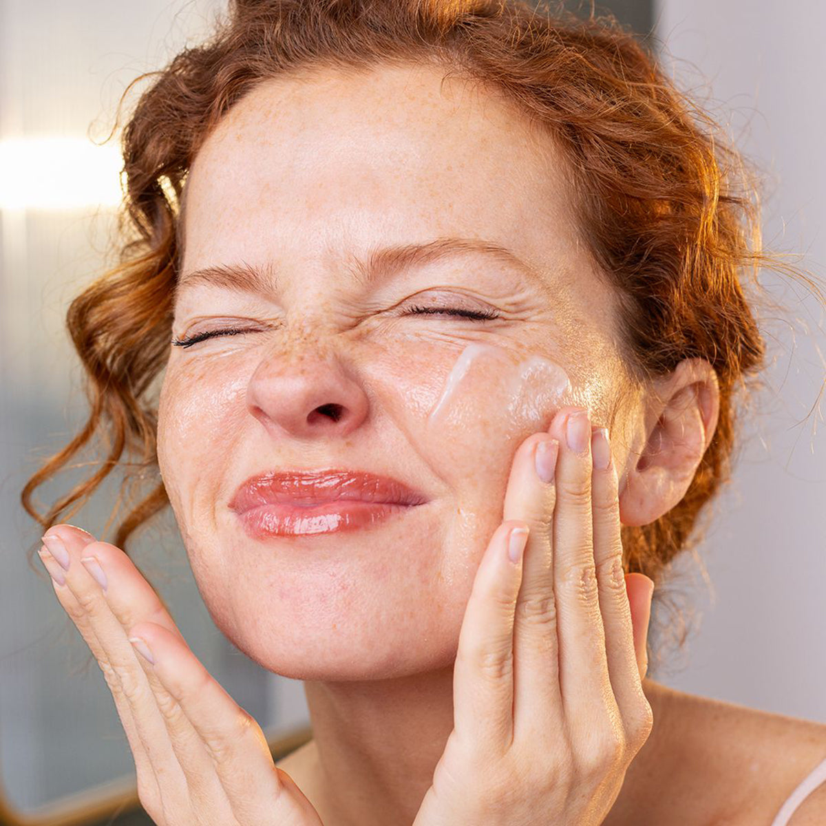Donna con capelli rossi applica il balsamo detergente SVR Sensifine sul viso, massaggiando la texture olio sulla pelle sensibile.