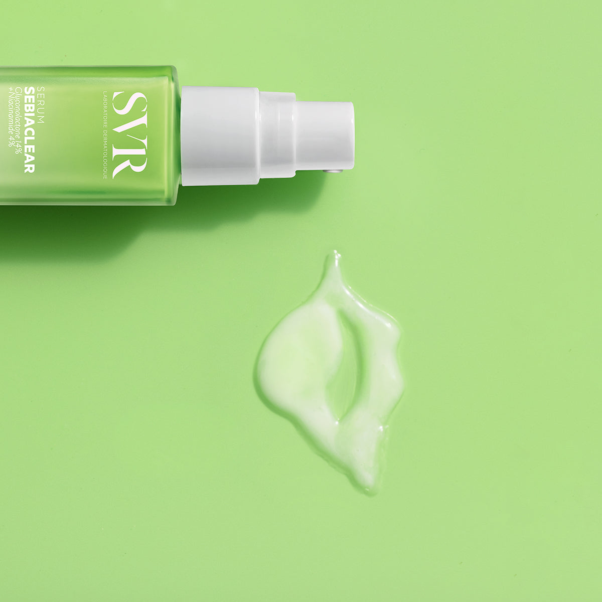 Flacone di siero SVR Sebiaclear verde con erogatore bianco e goccia di prodotto su sfondo verde chiaro.