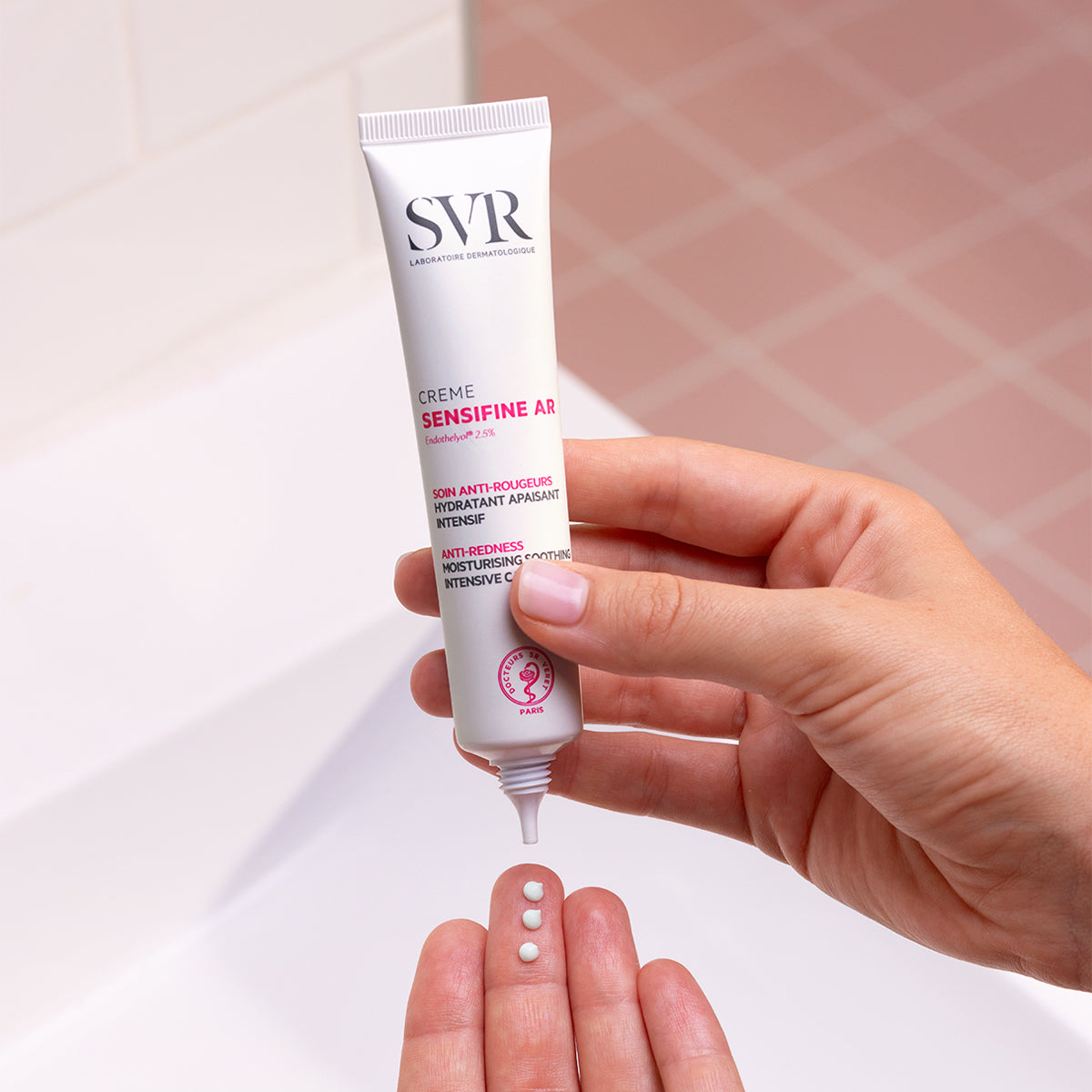 Tubo bianco di crema SVR Sensifine AR anti-rossore tenuto in mano con tre gocce di prodotto sul palmo.