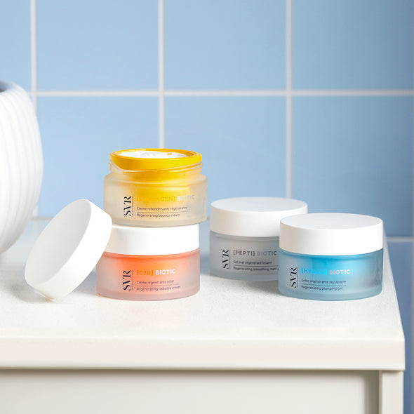 Barattoli di crema SVR Biotic colorati su un piano bianco davanti a piastrelle azzurre, inclusa la versione HYALU blu.