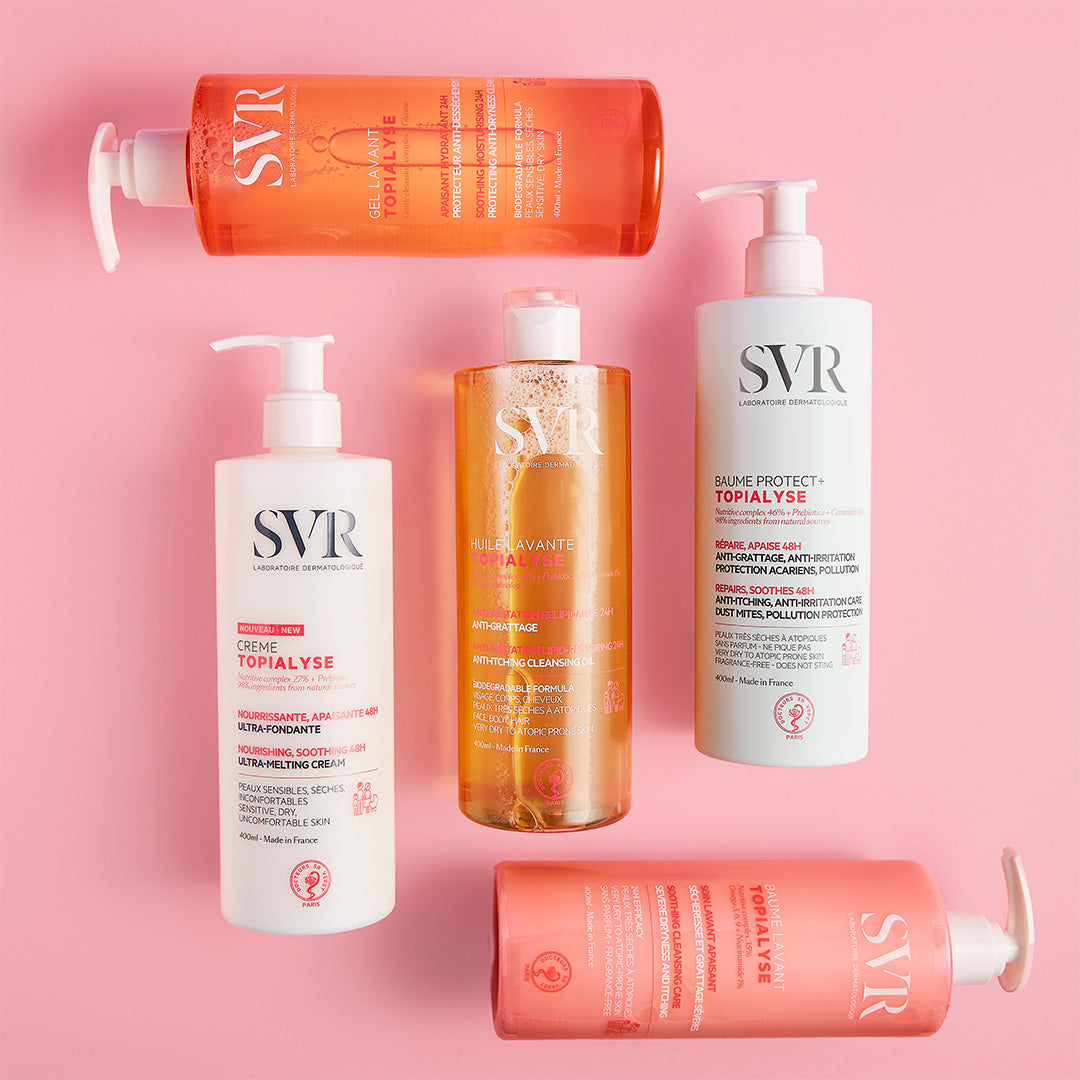 Cinque flaconi di prodotti SVR Topialyse con erogatore su sfondo rosa, tra cui creme e oli detergenti per pelli sensibili.