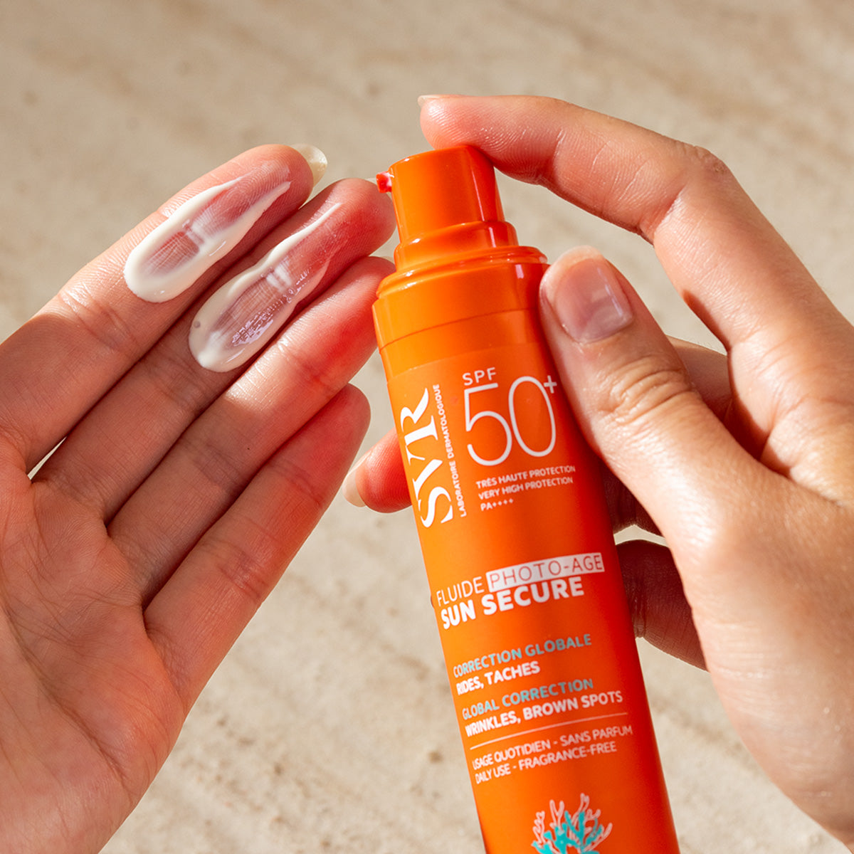 Mani che applicano il fluido solare SVR Sun Secure SPF50+ da un flacone arancione con texture cremosa bianca.