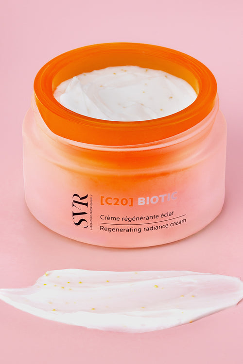 Vasetto di crema SVR [C20] Biotic in vetro satinato arancione con texture bianca cremosa su sfondo rosa.