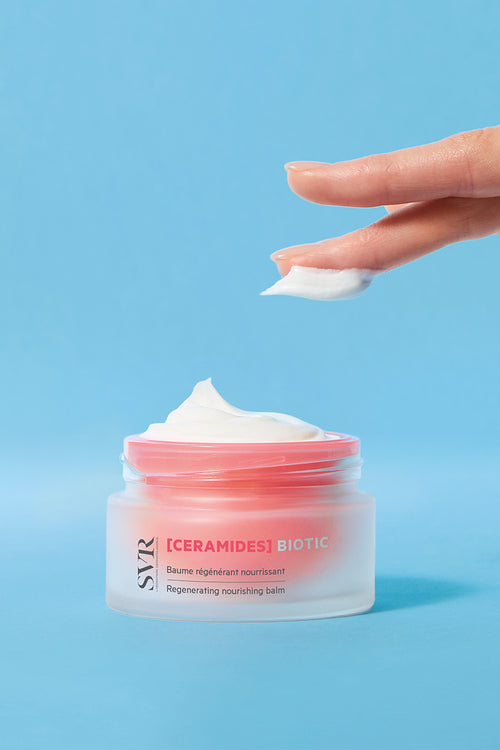 SVR [CERAMIDES] Biotic regenerating nourishing balm in a frosted glass jar with a pink lid against a blue background.