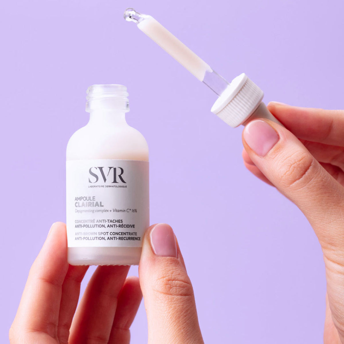 Flacone di SVR Clairial Ampoule anti-macchie in vetro satinato tenuto in mano con contagocce su sfondo lilla.