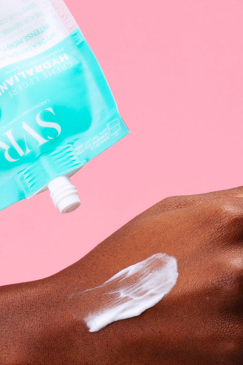 Tubetto SVR Hydraliane Crème Légère azzurro che applica una crema bianca sulla mano su sfondo rosa.