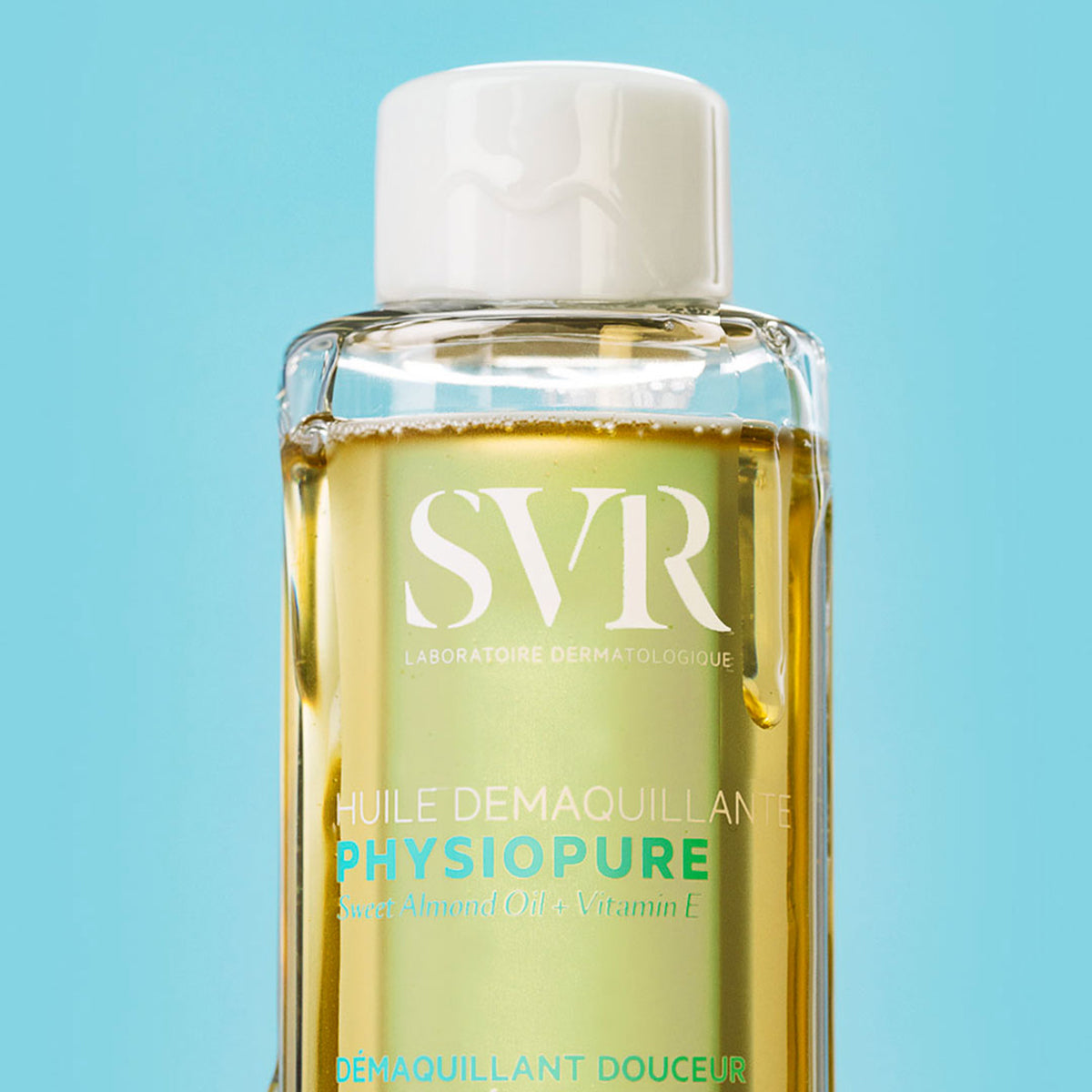 Flacone trasparente di SVR Physiopure Huile Démaquillante con olio dorato su sfondo azzurro.