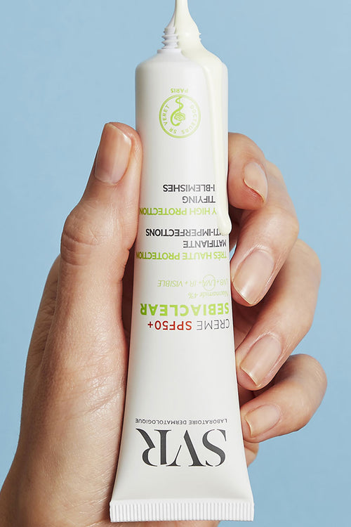 Mano che tiene un tubetto bianco di crema solare SVR Sebiaclear SPF50+ con texture fluida che fuoriesce dall'apertura.