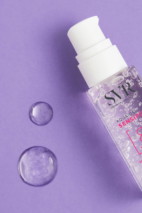 Flacone trasparente di SVR Sensifine Aqua-Gel con erogatore bianco su sfondo viola, accanto a due gocce di gel idratante.
