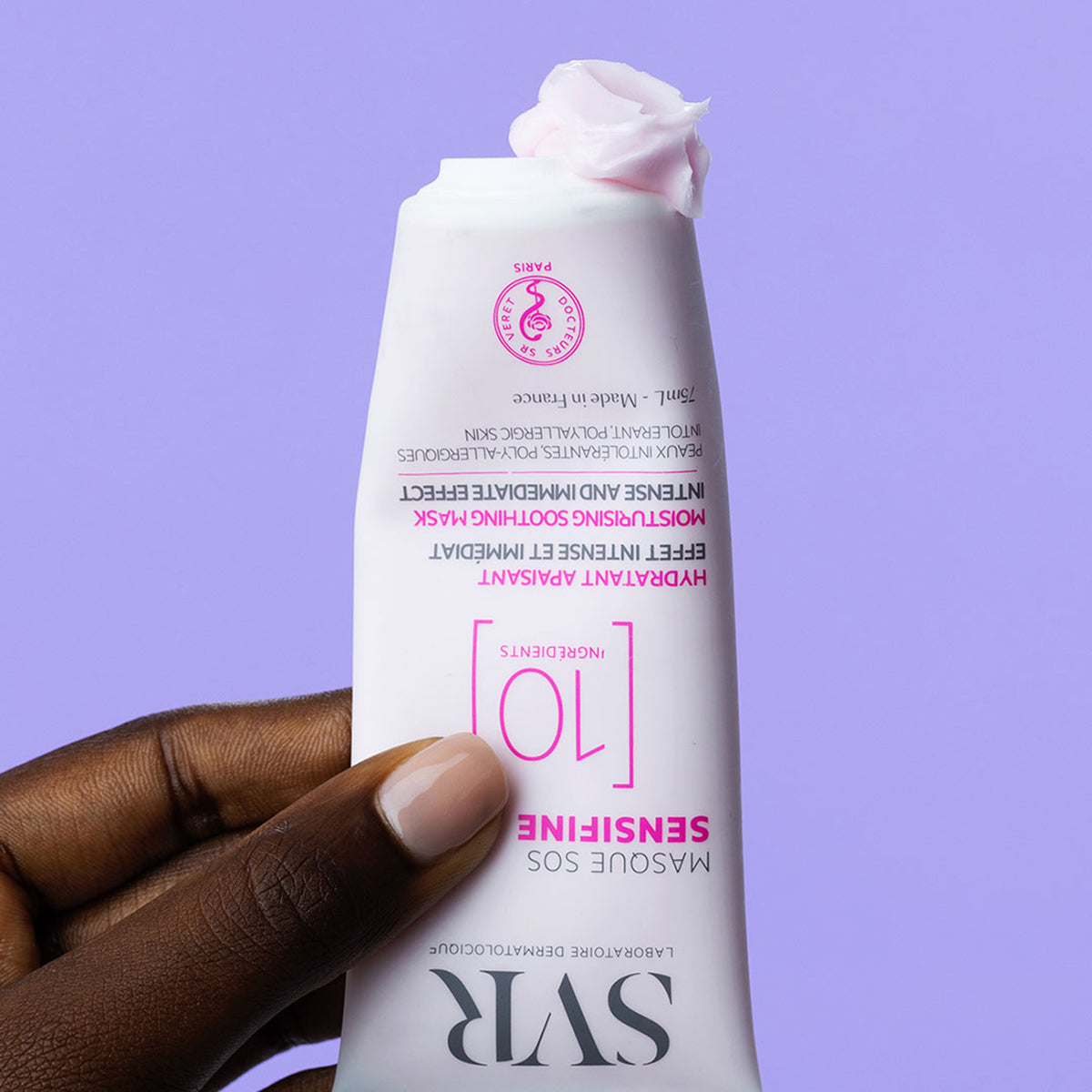 Tubo bianco di maschera SVR Sensifine SOS con crema rosa densa che fuoriesce, tenuto in mano su sfondo viola.