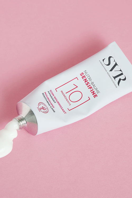 Tubo in alluminio SVR Sensifine Nutri-Baume con crema bianca che fuoriesce su sfondo rosa.