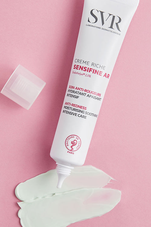 Tubo di crema SVR Sensifine AR Riche bianco con tappo aperto e una macchia di crema verde su sfondo rosa.