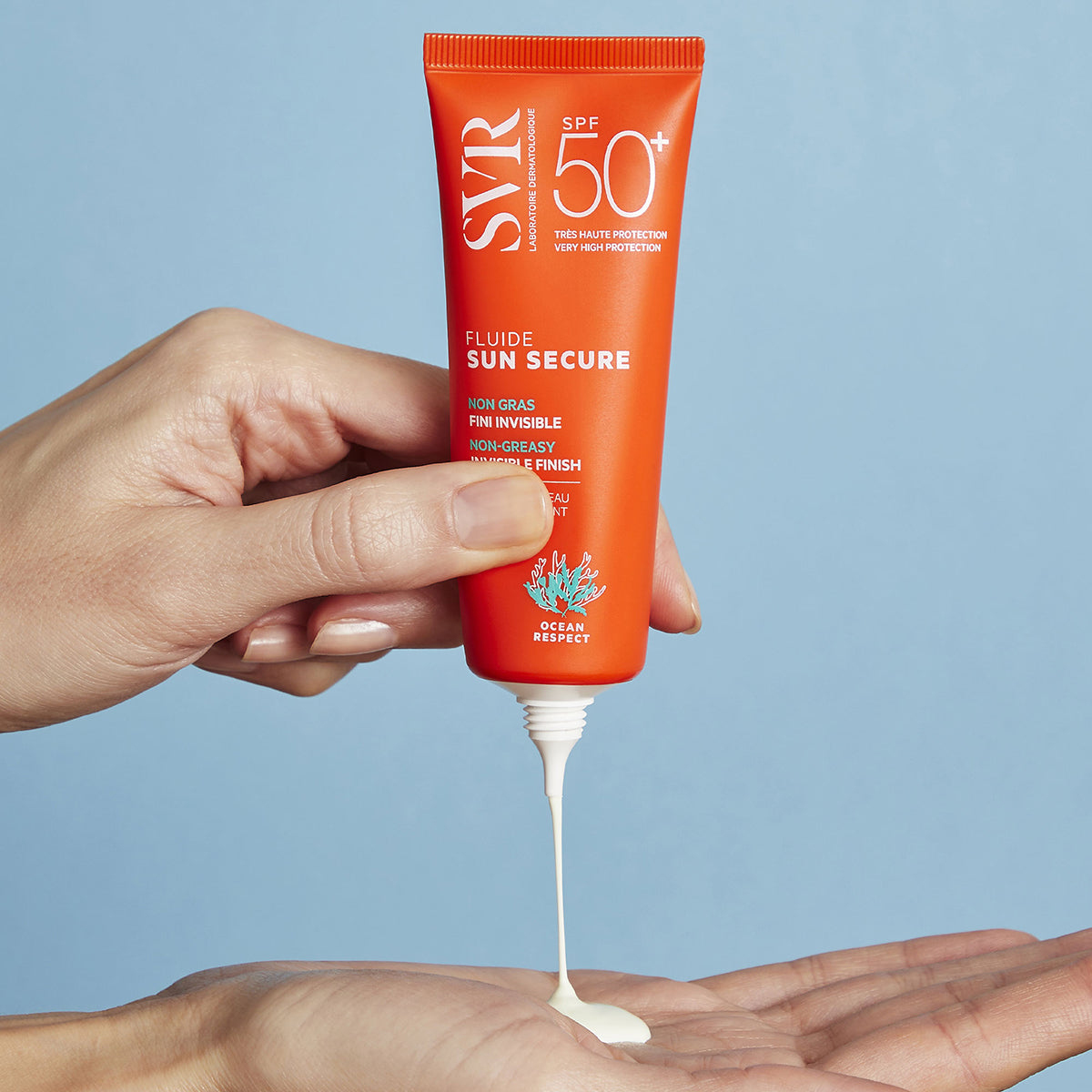 Tubo arancione di SVR SUN SECURE Fluide SPF50+ che eroga una crema solare fluida e bianca sul palmo di una mano.