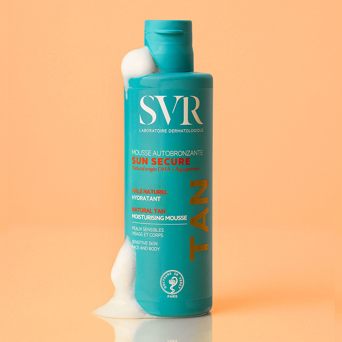 Flacone turchese di SVR Sun Secure Mousse Autobronzante con schiuma bianca su sfondo color pesca.