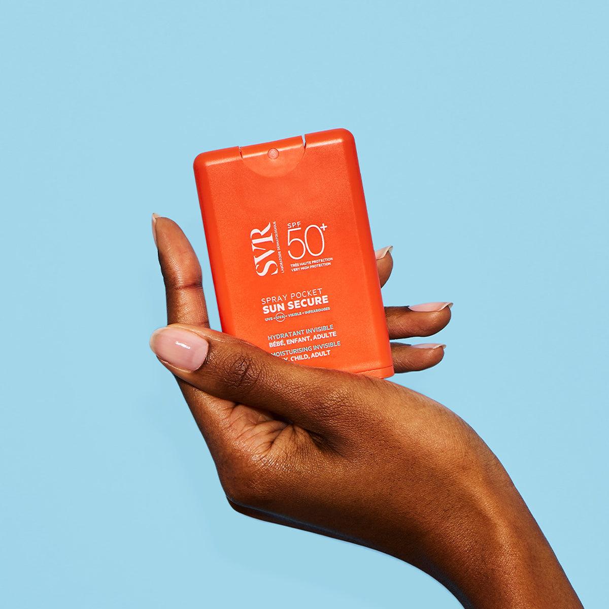 Mano che tiene il flacone spray tascabile arancione SVR Sun Secure SPF50+ su sfondo azzurro.