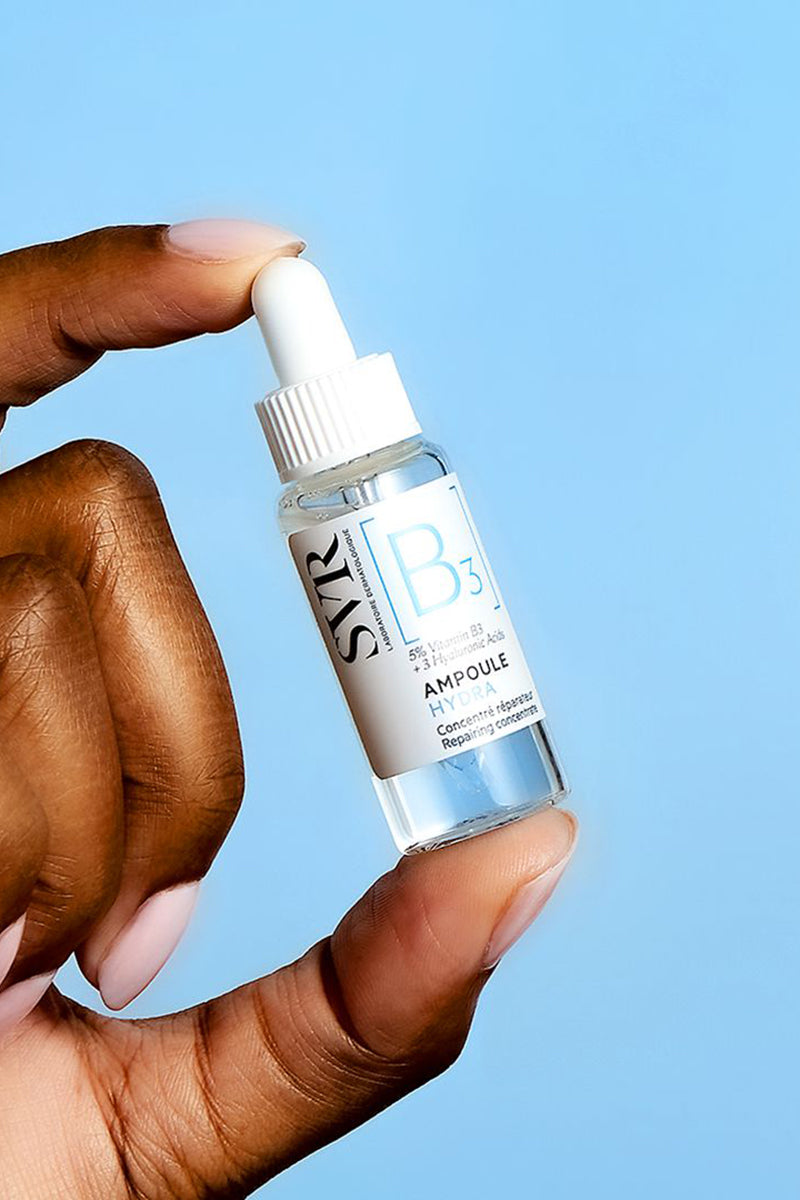 Mano che tiene un flacone di SVR Ampoule Hydra con contagocce bianco su sfondo azzurro.
