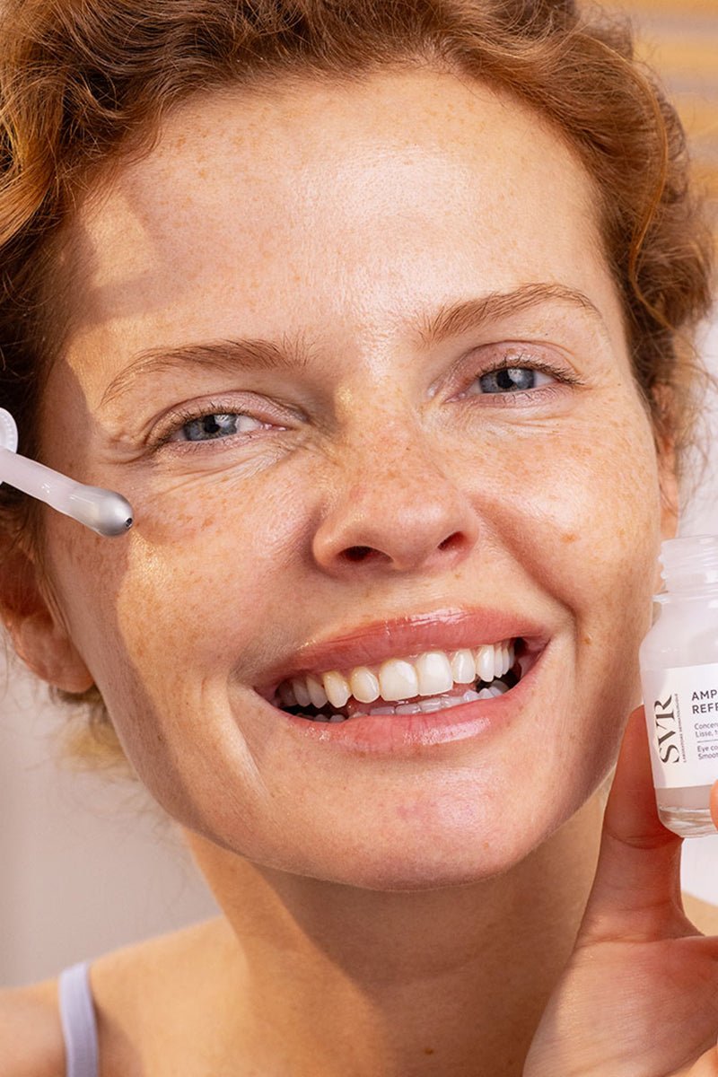 Donna sorridente applica il siero contorno occhi SVR Ampoule Refresh con l'innovativo applicatore in metallo rinfrescante.
