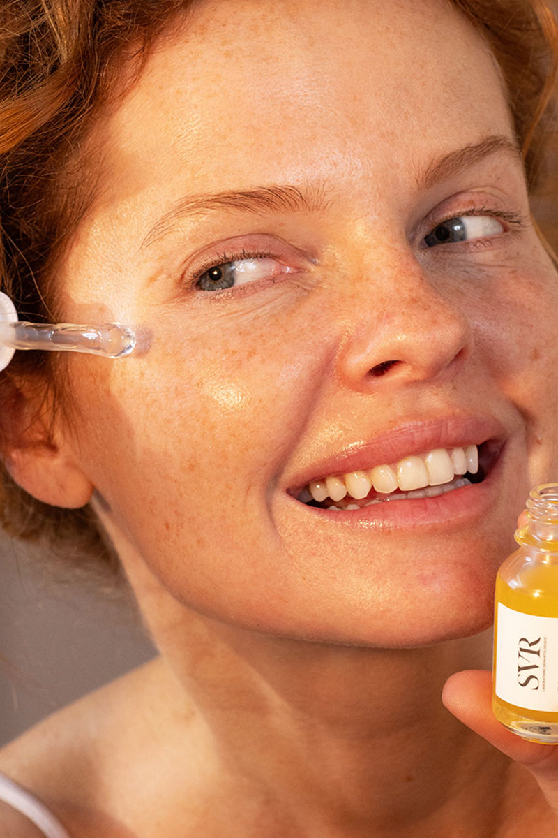 Donna sorridente applica il siero SVR Ampoule Relax sul contorno occhi con l'applicatore a pipetta in vetro.