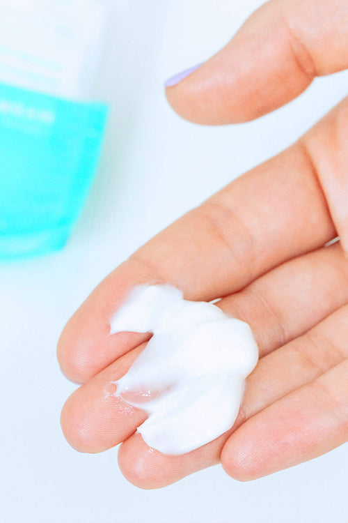 Crema viso bianca e ricca applicata sul palmo della mano con tubetto Hydraliane sullo sfondo.