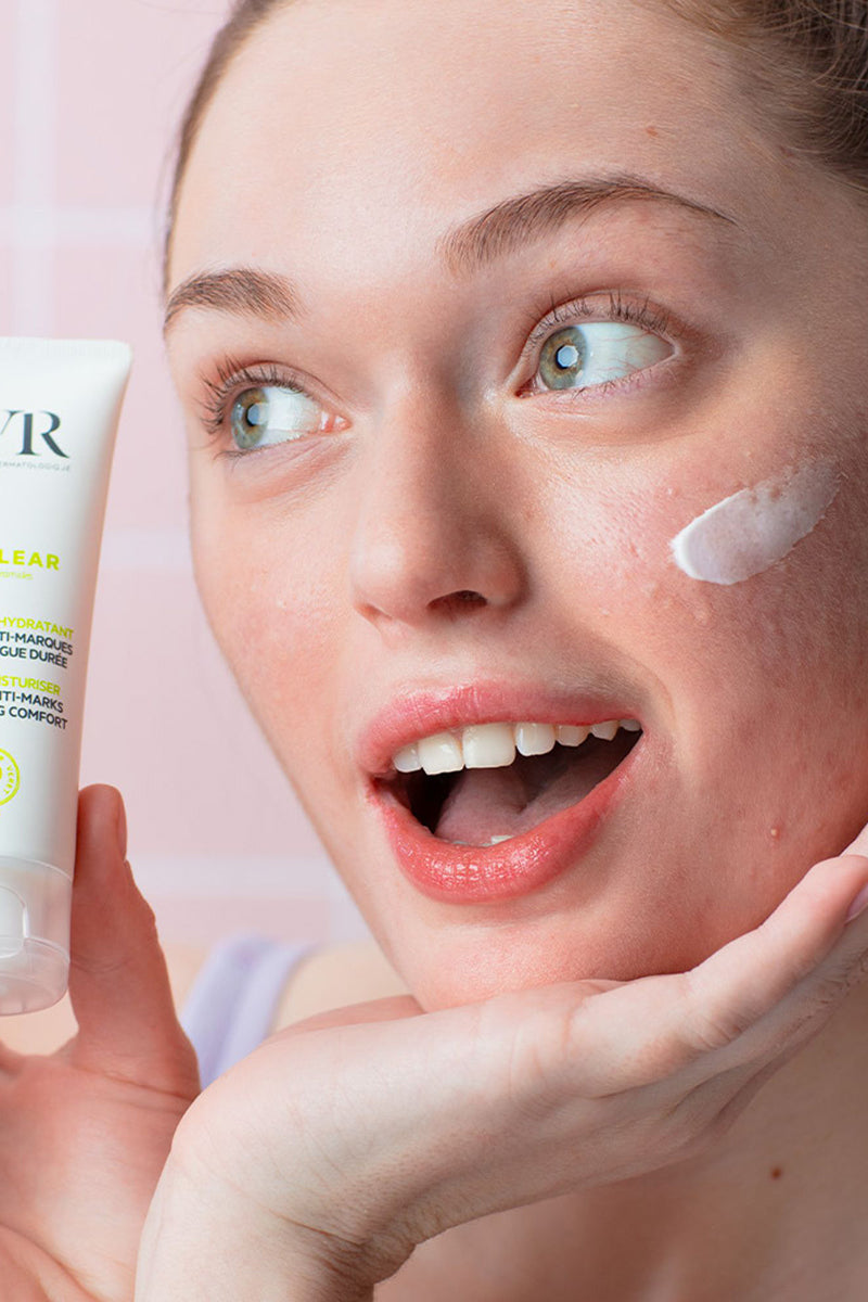 Donna che tiene in mano il tubetto bianco di SVR Sebiaclear Hydra con crema idratante applicata sulla guancia.