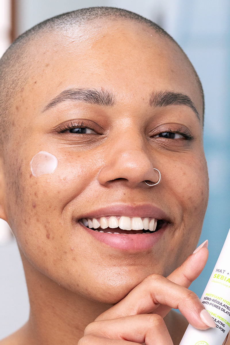 Donna sorridente con crema SVR Sebiaclear Mat+Pores sul viso, tubo bianco con scritte verdi e nere in primo piano.