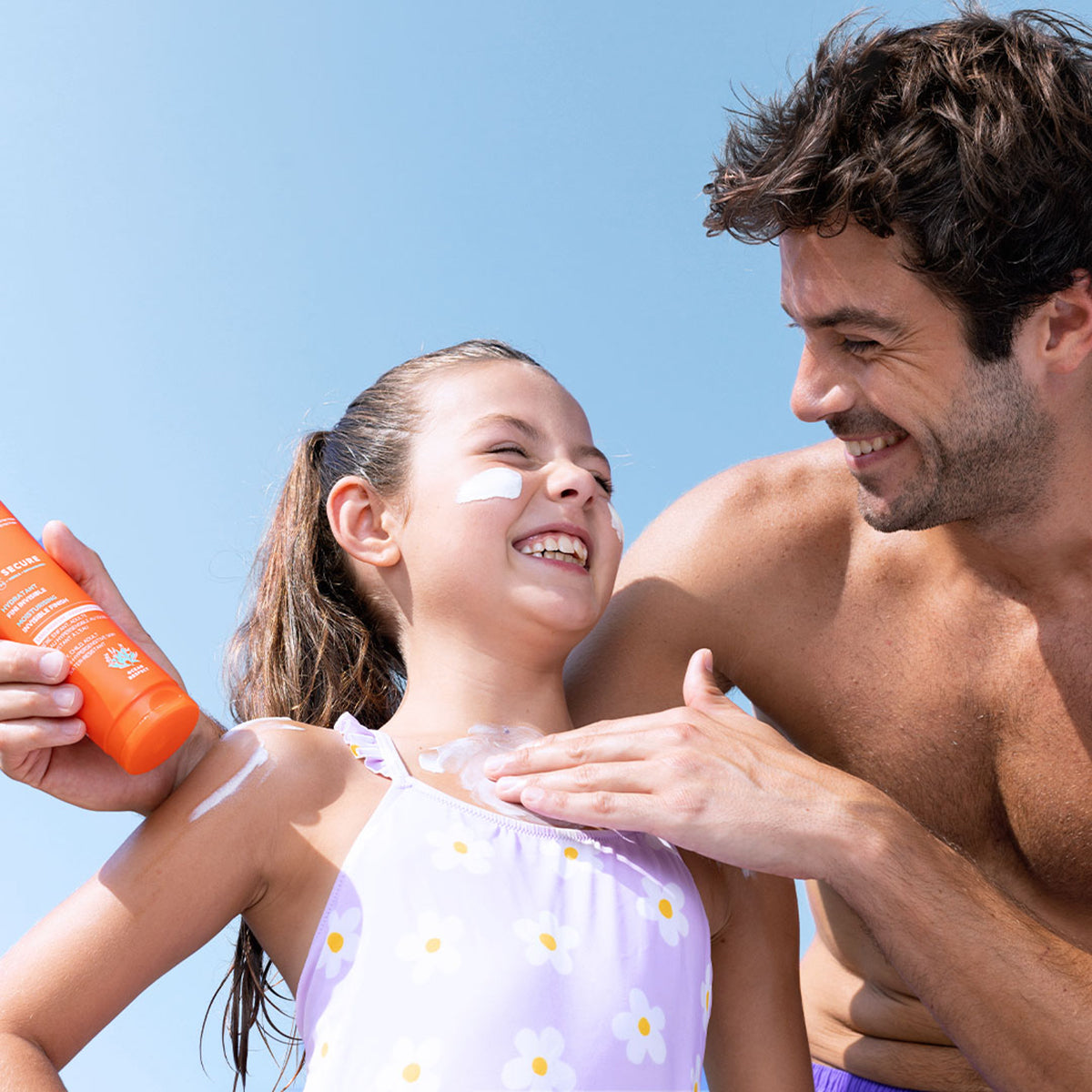 Padre applica la crema solare SUN SECURE SPF50+ sulla pelle della figlia in una giornata di sole all'aperto.