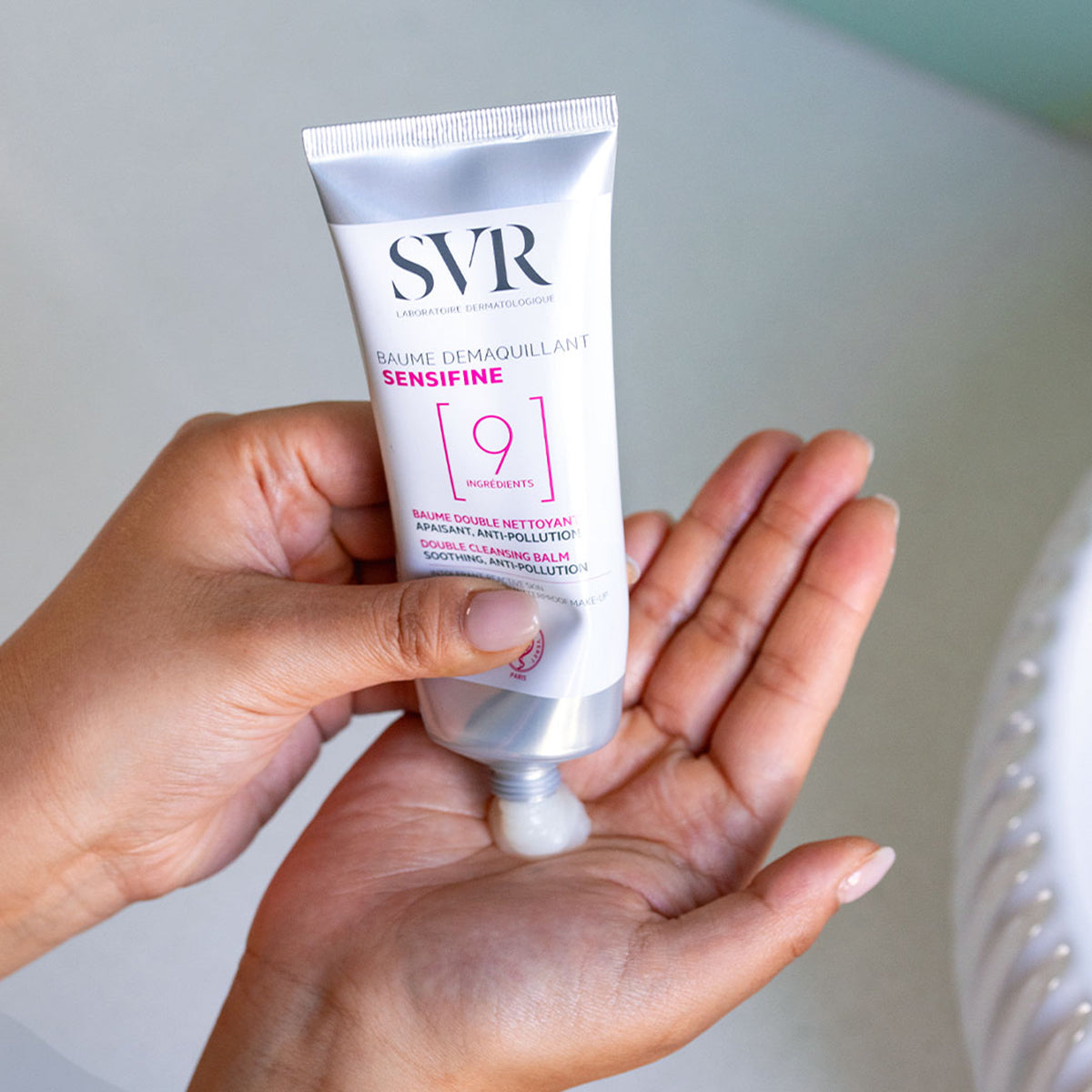 Tubo di SVR Sensifine Baume Démaquillant bianco e argento che eroga il balsamo detergente sul palmo della mano.