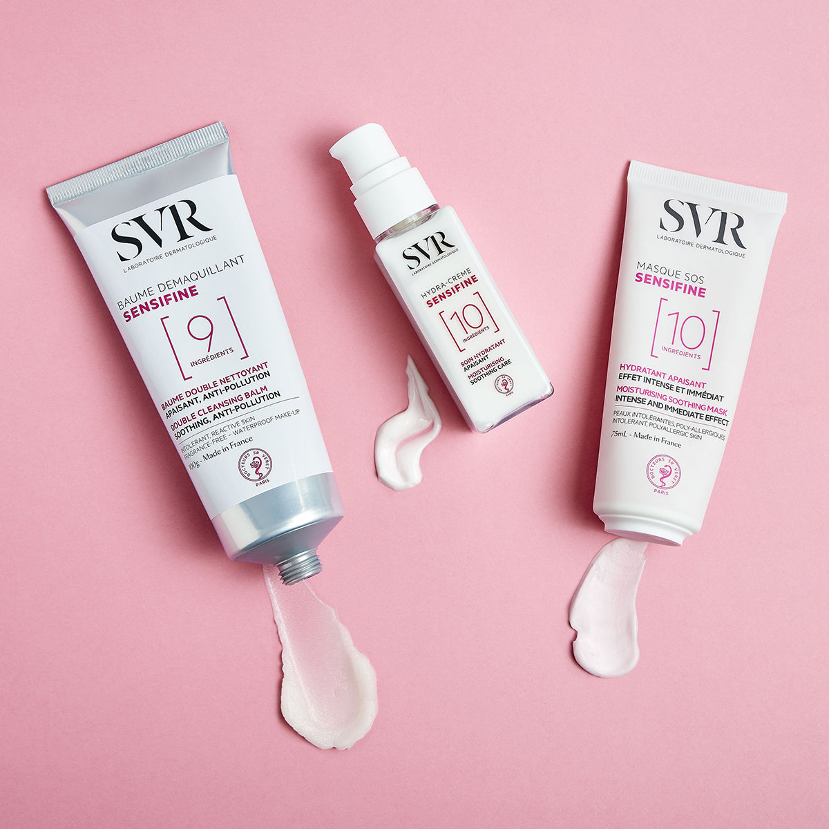 Tre prodotti SVR Sensifine bianchi con scritte rosa su sfondo rosa, con texture in crema che fuoriesce dai tubetti.