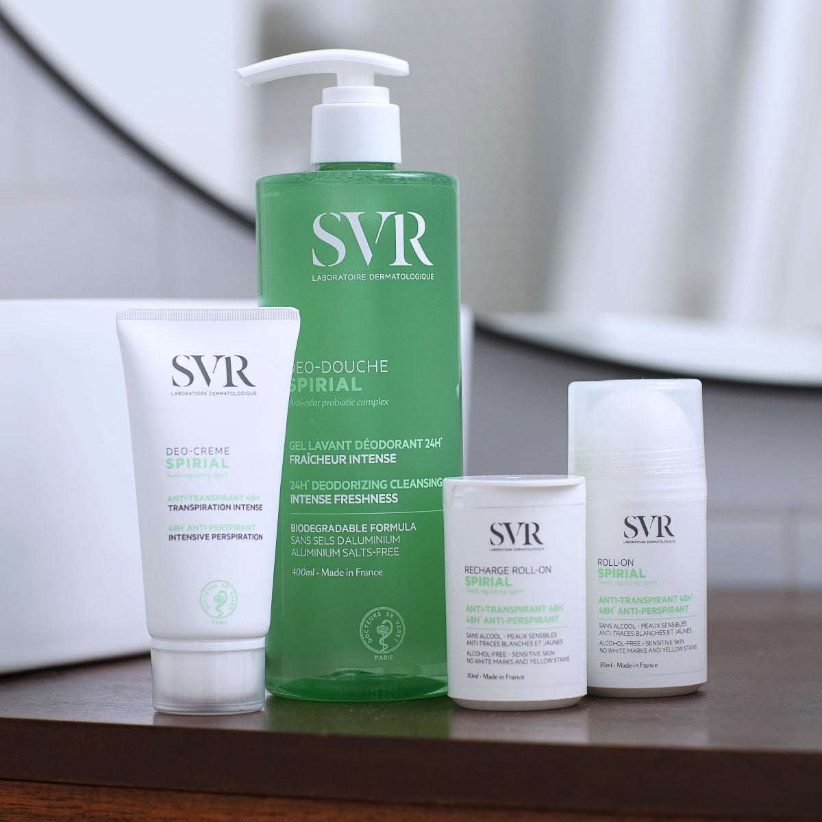 Gamma di prodotti SVR Spirial: un flacone verde di gel doccia e tre confezioni bianche di deodorante su una superficie scura.