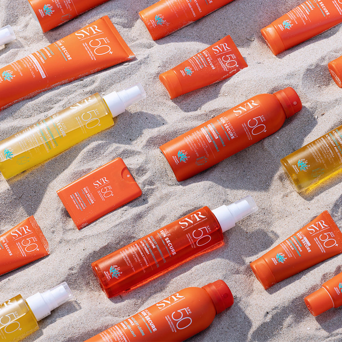 Vari flaconi e tubetti di protezione solare SVR Sun Secure SPF50+ disposti sulla sabbia di una spiaggia soleggiata.