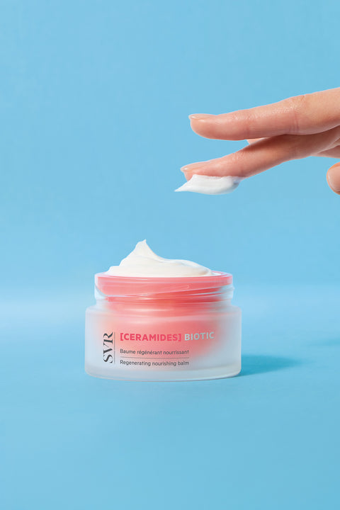 SVR Ceramides Biotic regenerating nourishing balm in a frosted glass jar with a pink lid against a blue background.