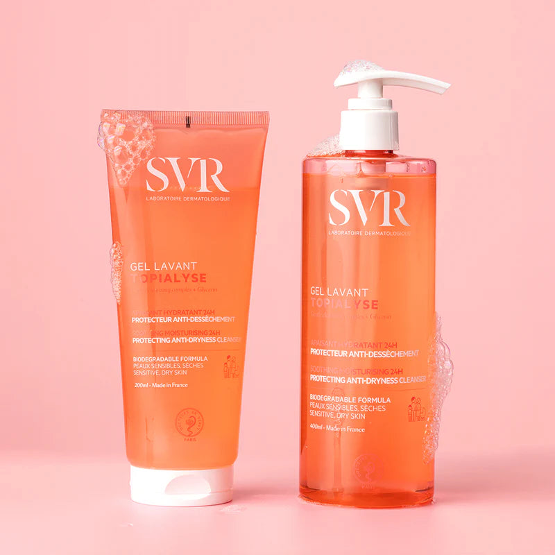 Flacone con erogatore e tubo di SVR Topialyse Gel Lavant arancioni su sfondo rosa con bolle di sapone detergenti.