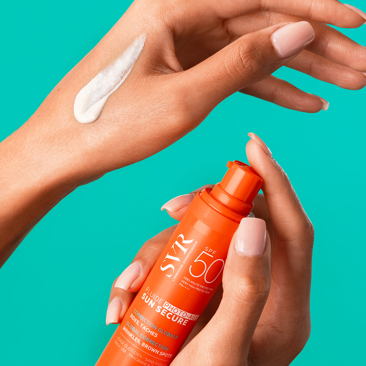 Flacone arancione di SVR Sun Secure Fluide Photo-Age SPF50+ tenuto in mano con una texture fluida bianca sulla pelle.