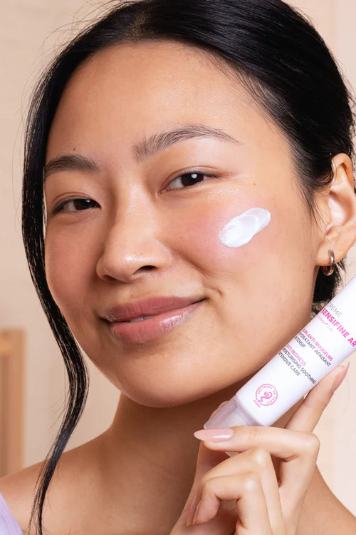 Donna sorridente che applica la crema viso SVR Sensifine AR, un tubetto bianco con scritte rosa per pelli reattive.
